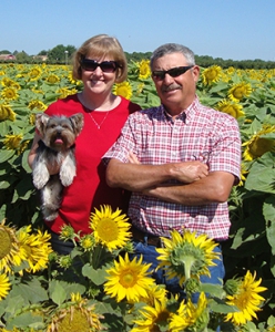 Helen with her husband and dog in a sunflower field.