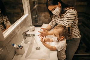 Mom and daugther wearing face masks washing their hands.