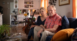 John and his wife sitting on their living room couch with guitar next to them.
