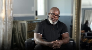 Bald man with a white beard sitting in his living room staring at the camera.